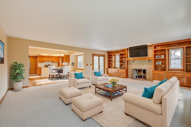 living room featuring built in shelves, an inviting chandelier, a brick fireplace, light carpet, and baseboards