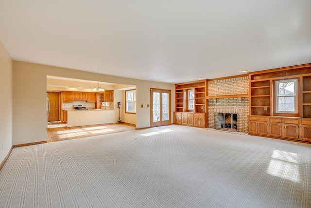 unfurnished living room with a chandelier, light colored carpet, a fireplace, built in features, and baseboards