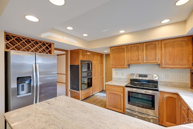 kitchen featuring black appliances, light stone counters, decorative backsplash, and light wood-style floors