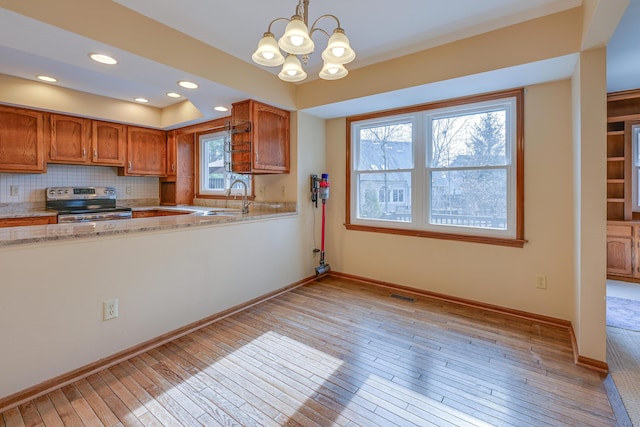 kitchen with electric stove, visible vents, decorative backsplash, brown cabinetry, and a sink