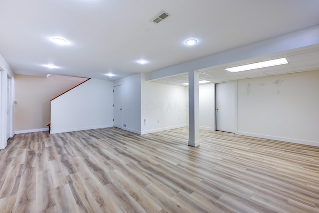 finished below grade area featuring a paneled ceiling, light wood-type flooring, visible vents, and baseboards