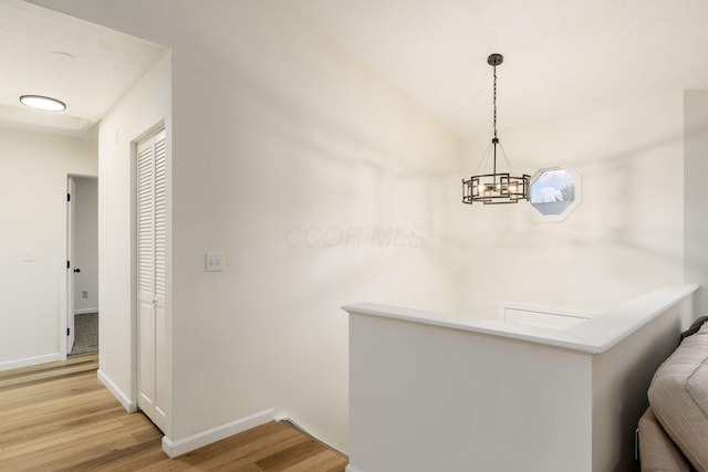 hall featuring light wood-style floors, baseboards, a notable chandelier, and an upstairs landing