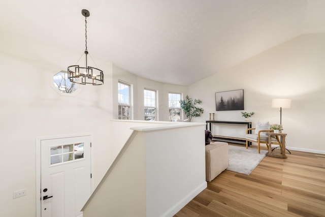 corridor with light wood finished floors, baseboards, an inviting chandelier, vaulted ceiling, and an upstairs landing