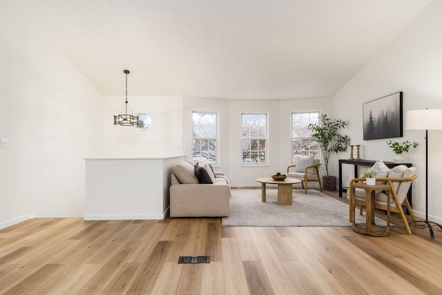 living area with light wood-style floors, baseboards, and an inviting chandelier