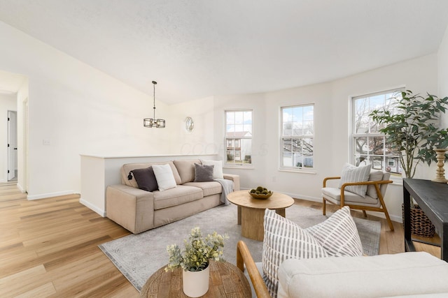 living room featuring lofted ceiling, light wood-style floors, baseboards, and an inviting chandelier