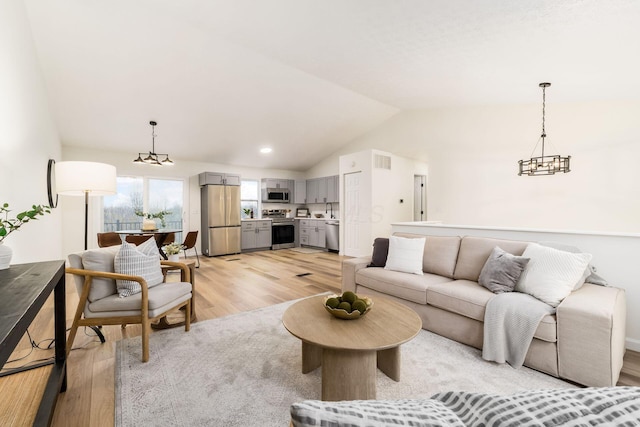 living area featuring lofted ceiling, light wood-style flooring, visible vents, and a chandelier