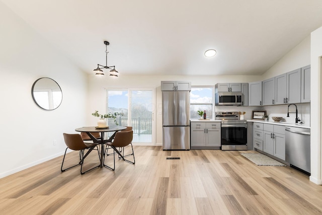 kitchen with light wood-style flooring, appliances with stainless steel finishes, vaulted ceiling, gray cabinets, and light countertops