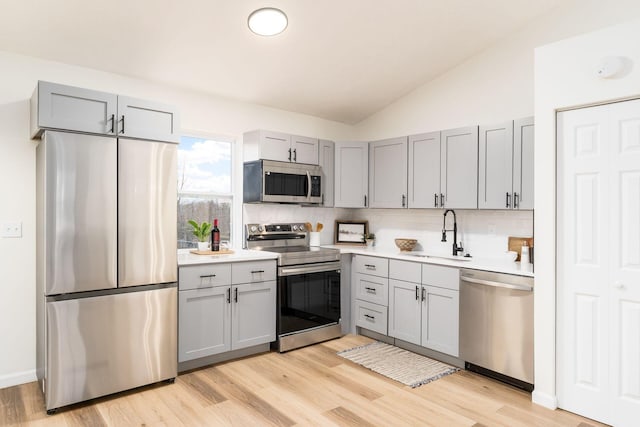 kitchen with stainless steel appliances, tasteful backsplash, gray cabinets, a sink, and vaulted ceiling