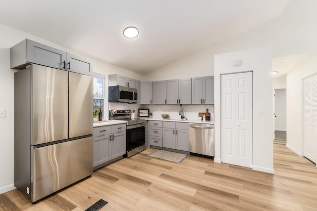 kitchen featuring lofted ceiling, stainless steel appliances, a sink, light countertops, and gray cabinets