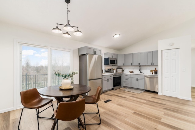 kitchen featuring stainless steel appliances, gray cabinets, light countertops, light wood-style flooring, and a sink