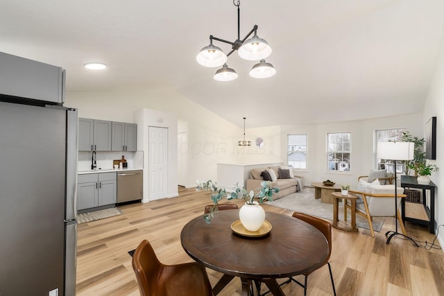 dining area featuring light wood-style floors, a chandelier, and vaulted ceiling