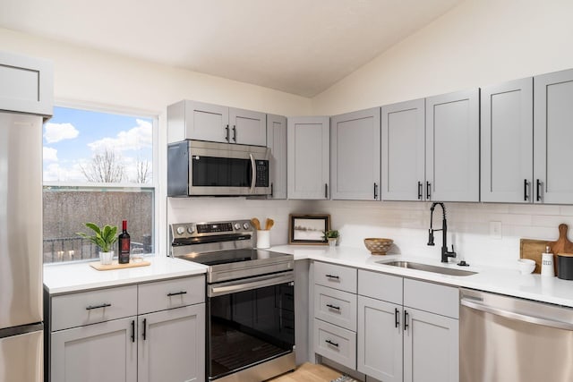 kitchen with stainless steel appliances, lofted ceiling, gray cabinets, and a sink