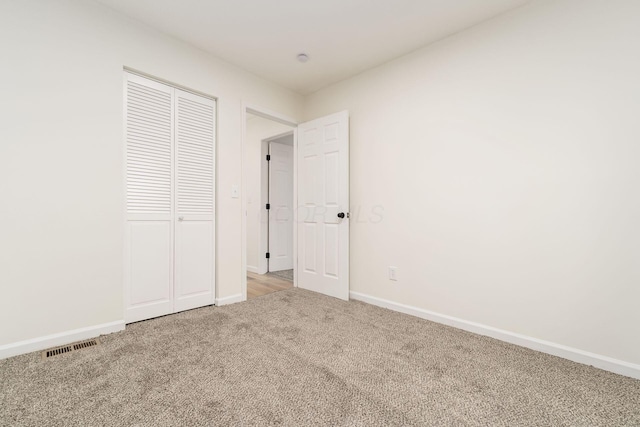 unfurnished bedroom featuring baseboards, visible vents, a closet, and light colored carpet