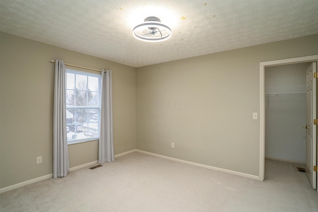 spare room featuring visible vents, light carpet, baseboards, and a textured ceiling