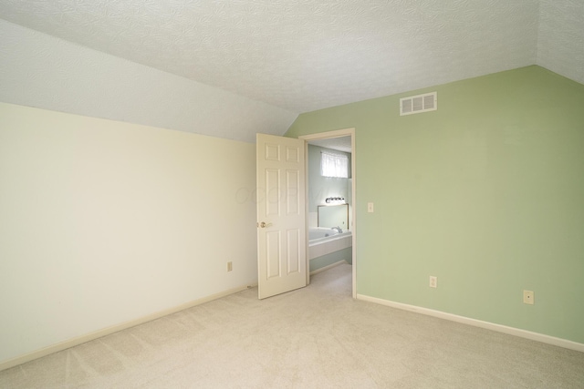 empty room featuring light carpet, a textured ceiling, lofted ceiling, and visible vents