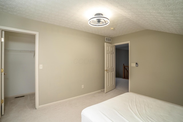 bedroom with light carpet, visible vents, a textured ceiling, and lofted ceiling