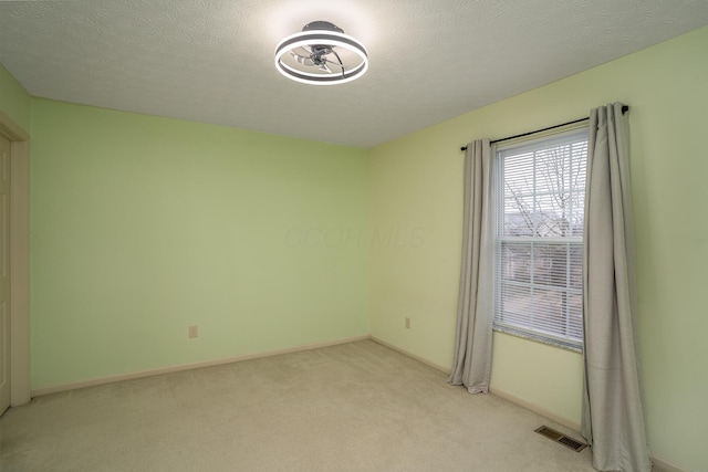 spare room featuring baseboards, visible vents, a textured ceiling, and light colored carpet