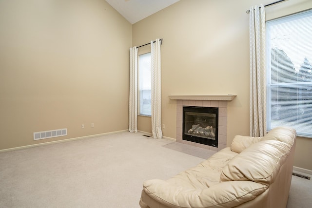 carpeted living area featuring baseboards, visible vents, vaulted ceiling, and a tiled fireplace