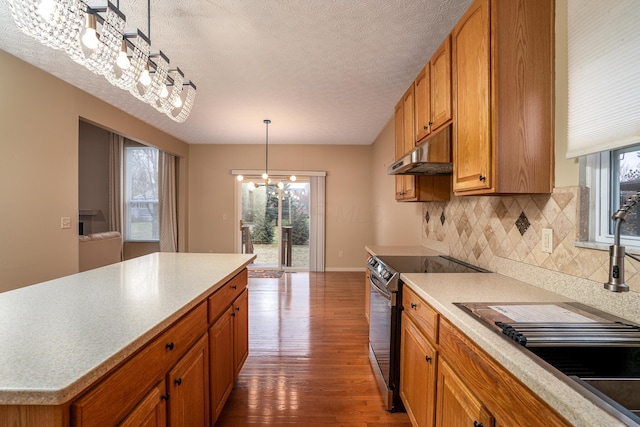 kitchen with under cabinet range hood, backsplash, stainless steel electric stove, dark wood-style floors, and brown cabinetry