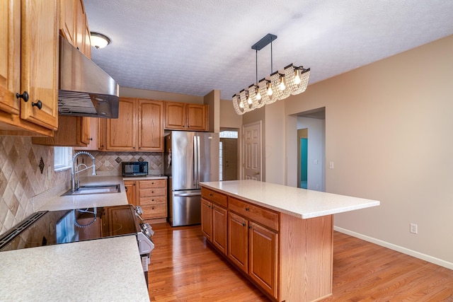 kitchen featuring extractor fan, a sink, light countertops, freestanding refrigerator, and tasteful backsplash