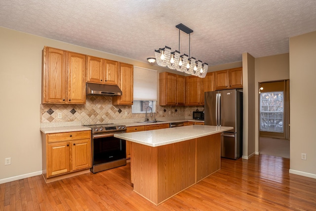 kitchen featuring decorative backsplash, appliances with stainless steel finishes, light wood-type flooring, under cabinet range hood, and a sink