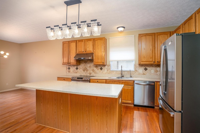 kitchen featuring light wood-style floors, stainless steel appliances, light countertops, under cabinet range hood, and a sink