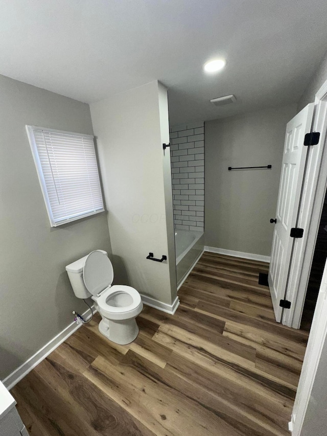 bathroom with baseboards, shower / bath combination, toilet, and wood finished floors