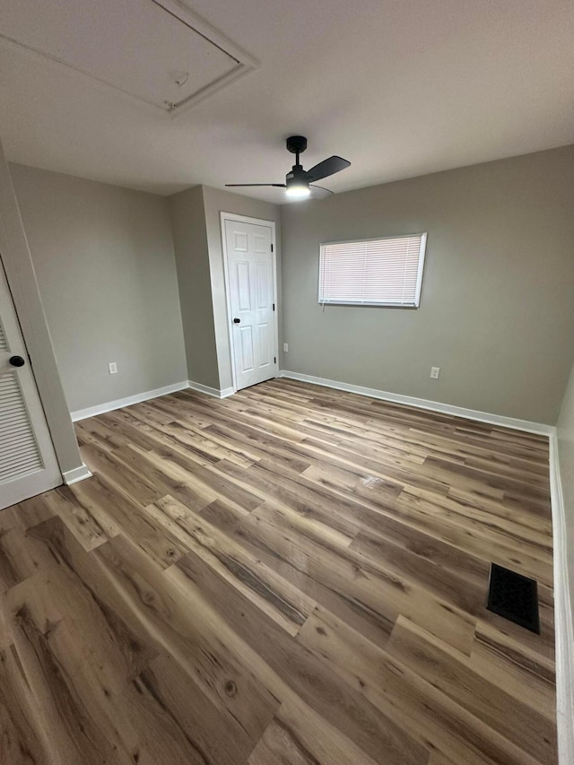 unfurnished bedroom featuring ceiling fan, wood finished floors, attic access, and baseboards