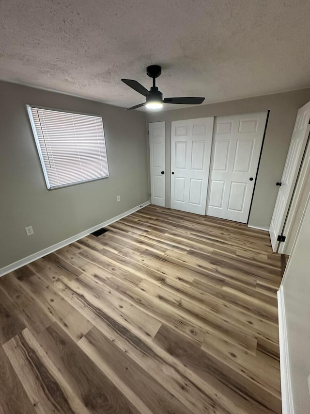 unfurnished bedroom featuring ceiling fan, a textured ceiling, baseboards, and wood finished floors