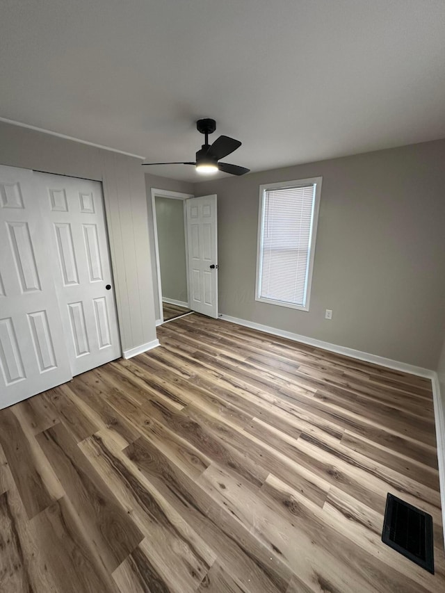 unfurnished bedroom featuring wood finished floors, a ceiling fan, visible vents, baseboards, and a closet