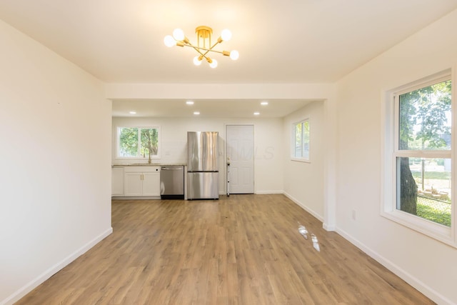 spare room with light wood finished floors, a notable chandelier, baseboards, and a sink