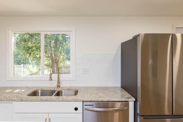 kitchen with a sink, light stone counters, white cabinetry, and stainless steel appliances