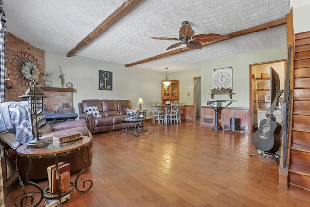 living room with a ceiling fan, a wainscoted wall, wood finished floors, a textured ceiling, and beam ceiling