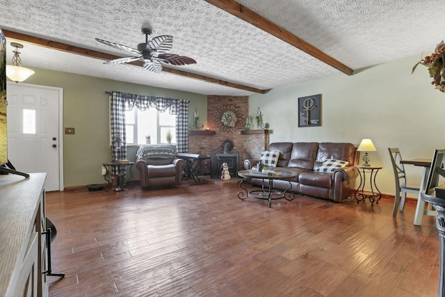 living room with a ceiling fan, wood finished floors, a wood stove, a textured ceiling, and beam ceiling