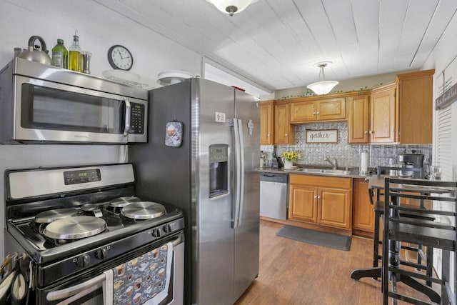 kitchen featuring tasteful backsplash, appliances with stainless steel finishes, brown cabinets, wood finished floors, and a sink