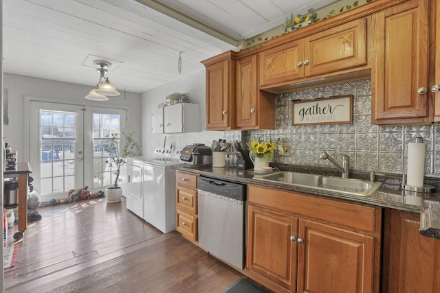 kitchen with tasteful backsplash, washer and clothes dryer, brown cabinets, stainless steel dishwasher, and a sink