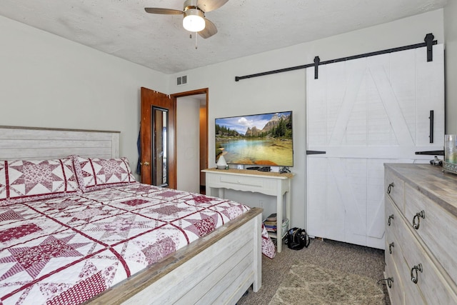 bedroom with carpet floors, visible vents, a barn door, a ceiling fan, and a textured ceiling