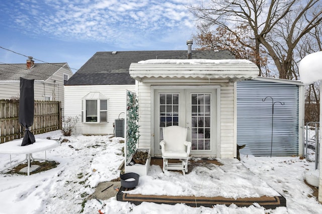 snow covered back of property featuring french doors, roof with shingles, fence, and central air condition unit