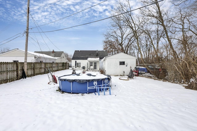 snow covered back of property featuring an outdoor structure, fence, and a fenced in pool