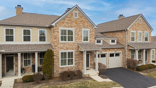 view of front of home featuring roof with shingles, a chimney, covered porch, an attached garage, and driveway