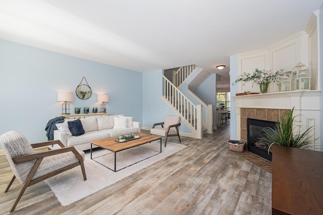 living room with light wood-style flooring, stairway, and a tiled fireplace