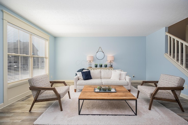 living area with a textured ceiling, stairway, wood finished floors, and baseboards