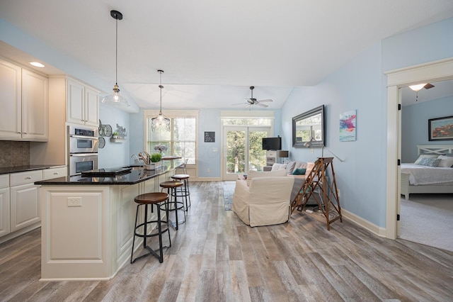 kitchen with lofted ceiling, light wood-style flooring, double oven, open floor plan, and a kitchen bar