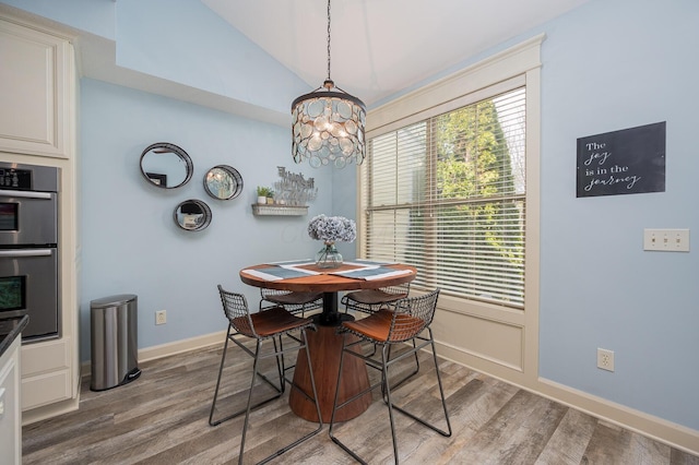 dining space featuring vaulted ceiling, a notable chandelier, wood finished floors, and baseboards