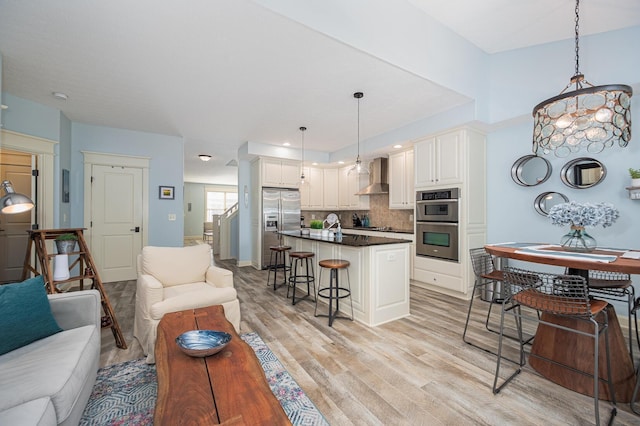 kitchen with light wood finished floors, dark countertops, wall chimney exhaust hood, appliances with stainless steel finishes, and open floor plan