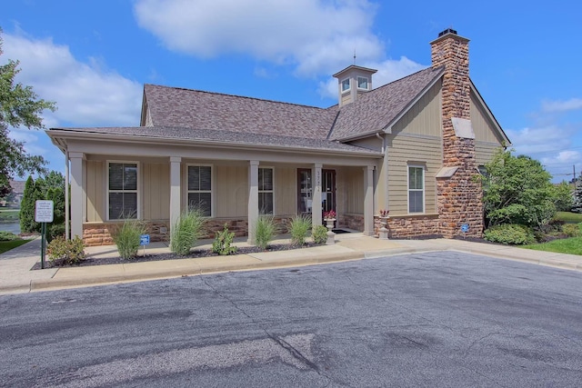 view of front of property with stone siding, a chimney, roof with shingles, covered porch, and board and batten siding