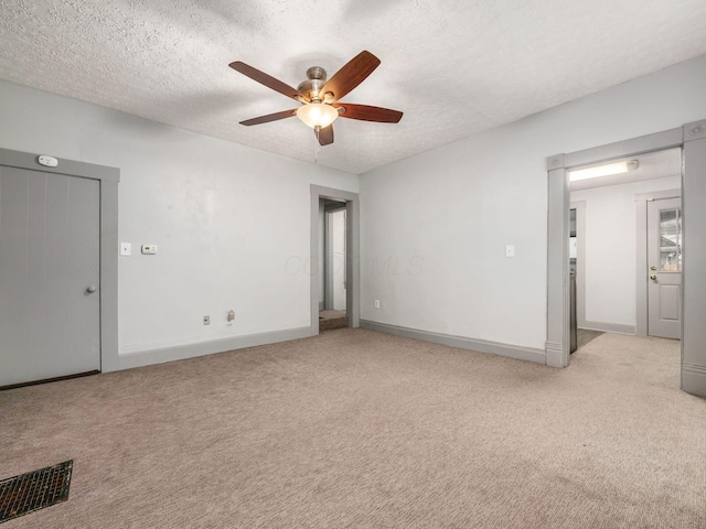 empty room featuring light carpet, a ceiling fan, visible vents, and a textured ceiling