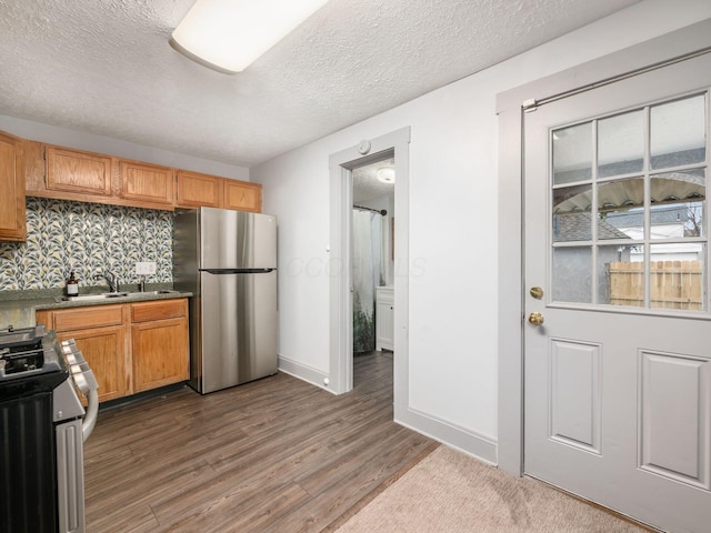 kitchen with a textured ceiling, stainless steel appliances, a sink, wood finished floors, and baseboards