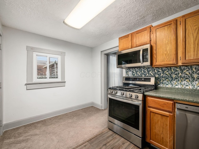 kitchen featuring a textured ceiling, appliances with stainless steel finishes, brown cabinetry, and baseboards