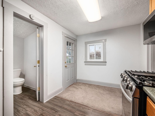 interior space featuring a textured ceiling, appliances with stainless steel finishes, wood finished floors, and baseboards